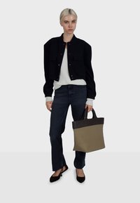 Zwarte korte jas, crèmekleurige trui, donkere jeans en zwarte platte schoenen. Draagt een gestructureerde totebag in bruin en beige. Eenvoudig, modern ontwerp.