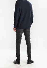 Marinblå stickad tröja med rundad halsringning, kombinerad med mörkgrå avsmalnande jeans och svarta ankelstövlar.