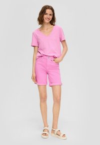 Roze T-shirt met korte mouwen en V-hals, gecombineerd met roze shorts met opgerolde zoom, gedragen met lichtgekleurde plateausandalen. Glad, casual textuur van de stof.