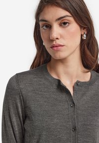 Dunkelgrauer Cardigan mit rundem Halsausschnitt, Knopfverschluss und langen Ärmeln. Weiche Textur mit figurbetonter Silhouette.