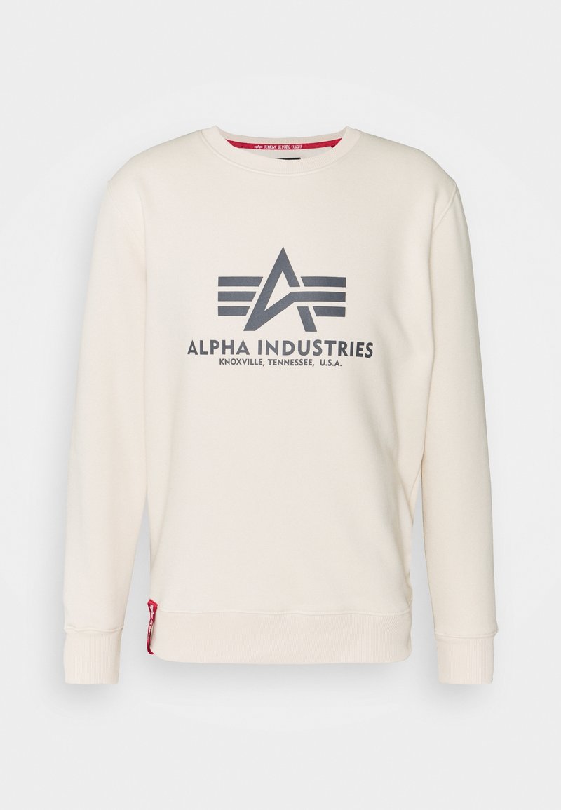 Sweat-shirt crème à col rond avec manches longues, affichant un grand logo Alpha Industries gris foncé et un texte sur le devant.