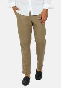 Chino beige con vestibilità dritta e orli risvoltati, realizzati in tessuto traspirante. Indossati con scarpe tipo mocassino nere. Camicia bianca con bottoni.