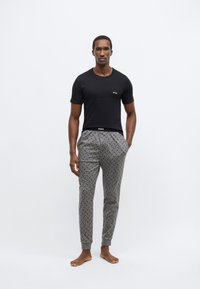 Fekete rövid ujjú ing kis fehér logóval, szürke mintás joggingnadrággal párosítva, mely fekete díszítéseket és bordázott mandzsettákat tartalmaz.