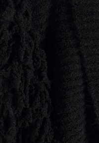 Musta neulottu kangas, jossa on erilaisia tekstuureja; toisella puolella kangas on sileä, kun taas toisella on silmukoinnin ja pörröisyyden yhdistelmä, joka luo kontrastoivaa syvyyttä.