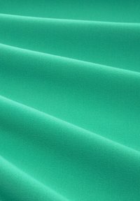 Tissu vert texturé avec une surface lisse, présentant des plis qui créent un motif ondulant, mettant en valeur sa qualité douce et flexible.