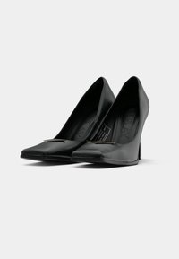 Scarpe nere con tacco alto, dalla punta appuntita, in materiale sintetico liscio, con un accento metallico sulla parte anteriore. Progettate con una silhouette elegante.