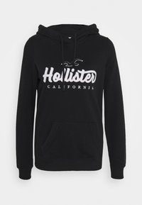 Felpa nera in morbido tessuto, dotata di tasca a marsupio frontale, cappuccio regolabile con cordini e logo "Hollister California" ricamato in bianco.