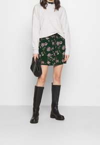 Grå sweatshirt, grön blommig minikjol, svarta knähöga stövlar och en svart clutch. Kjolen har ett botaniskt mönster med en knytning i midjan.