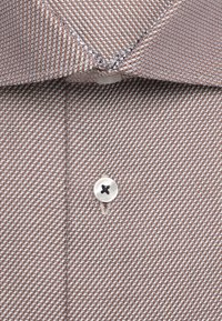 Gros plan du col d'une chemise marron à motifs avec un seul bouton blanc fermé à l'avant.