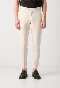 Slim-fit ljusbeige byxor i lätt material, med slät framsida, sidfickor och en knappstängning. Matchas med svarta loafers.