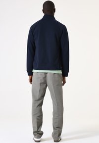 Navyblaue Jacke mit Stehkragen, gerippten Bündchen und lockerer Passform, kombiniert mit hellgrauen Hosen und weißen Sneakern.