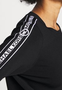 Pull noir à col rond, avec des accents rayés blancs sur les manches. Un détail de logo le long de la rayure met en valeur la marque.
