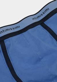 Blå bomullskalsonger med svart elastisk midjeband med "intimissimi"-logotyp och kontrasterande mörka sömmar. Slät textur och åtsittande design.