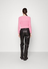 Růžový pletený svetr s dlouhými rukávy a žebrovaným lemem, spojený s černými kalhotami z umělé kůže s vysokým pasem. Hladká textura a elegantní design.