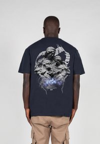 Svart bomulls t-skjorte med et detaljert grafisk design av to figurer omgitt av skyer og lyn, med tekstelementer tydelig vist.