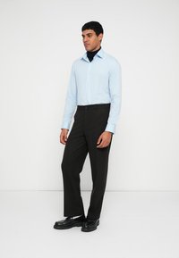 Light blue button-up shirt layered over a black turtleneck, paired with dark trousers and black shoes. Simple design and relaxed fit.