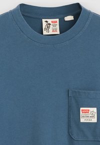 Blaues Baumwoll-T-Shirt mit Rundhalsausschnitt und kurzen Ärmeln. Verfügt über eine Brusttasche mit einem Etikett, das "Levi's", "Western Wear" und "Pixar" zeigt.