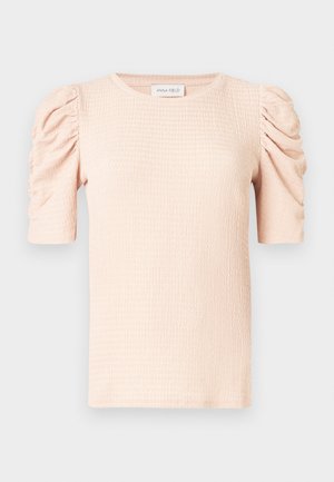 Blouse rose clair à manches courtes avec épaules bouffantes, tissu texturé et encolure ronde. L'étiquette indique "ANNA FIELD".