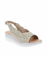 Sandal in pelle beige con design a ritagli, punta aperta, cinturino alla caviglia regolabile e suola a zeppa bianca. Texture liscia e dettagli minimi.