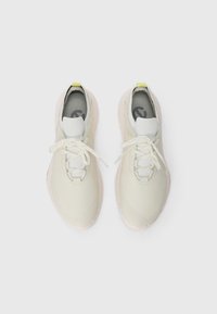Ljusgrå sneakers med en texturerad ovandel, rosa sula och vita snören. Har en minimalistisk design och en liten gul accent på hälkappan.