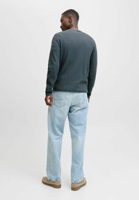 Pull en maille texturé gris foncé avec un col rond, associé à un jean ample bleu clair et des chaussures beiges. Arrière-plan épuré.