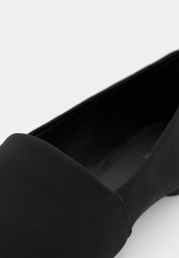 Chaussure plate noire à bout pointu avec une finition mate lisse et un petit talon sur un fond clair.