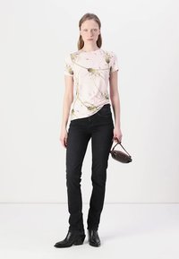 Camiseta rosa de manga curta com estampado floral, usada com jeans pretos e botas de salto pretas. A modelo segura uma pequena bolsa castanha.