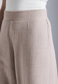 Světlá béžová žebrovaná sukně s vysokým pasem a jemnou texturou, s vertikálními pruhy a sklady pro zvýšenou detailnost.
