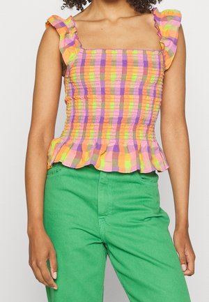 Haut smocké multicolore en motifs à carreaux violet, rose, orange et citron vert, avec des bretelles volantes et un ourlet en peplum, associé à un pantalon vert.