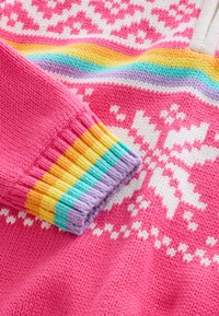 Neulepusero kirkkaan pinkkinä, jossa valkoinen lumihiutalekuvio. Moniväriset resorit hihansuissa, jotka sisältävät keltaisia, oransseja, vihreitä, purppuran ja sinisen sävyjä.