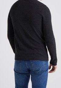 Mörkgrå långärmad tröja med rund halsringning, figurnära passform och slät textur, kombinerad med blå denimjeans.