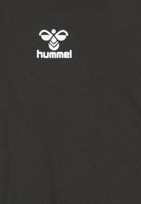 Białe stylizowane logo trzmiela z napisem „hummel” poniżej na czarnej tkaninie.