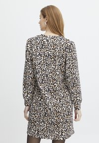 Haljina s uzorkom leoparda s dugim rukavima, svijetlo bež tkanina, crne i smeđe mrlje, opušteni kroj, doseže iznad koljena, jednostavni okrugli izrez.