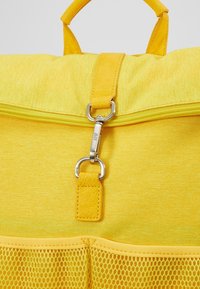 Bolsa de tela amarilla con un acabado texturizado, que presenta un cierre de cremallera, herrajes metálicos y un bolsillo de malla en la parte inferior.