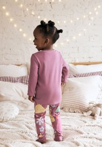 Lilla langærmet top kombineret med mønstrede leggings med blomstermotiver og prinsessegrafik. Blødt stof, afslappet pasform.