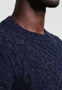 Granatowy sweter dzianinowy z teksturowanym wzorem w warkocze, wykonany z miękkiej przędzy, z okrągłym dekoltem oraz drobnymi akcentami kontrastowych kolorów.