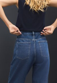 Blå denimjeans med høj talje, to baglommer, en glat tekstur og synlige syninger.