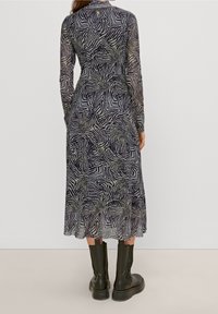 Vestido de manga larga en tela transparente con un patrón de cebra en blanco y negro, con una cintura ajustada y un dobladillo acampanado, combinado con botas negras hasta el tobillo.