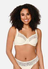 Reggiseno in pizzo crema con motivi floreali, coppe semitrasparenti e spalline regolabili. Include un bordino in pizzo abbinato sulla fascia.