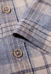 Camicia a quadri con un motivo blu e bianco. Tessuto morbido con bottoni e dettagli ai polsini. Design del colletto classico.