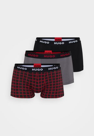 Kolme paria Hugo miesten bokserihousuja: mustat, harmaat ja punainen ruutukuosi mustalla pohjalla. Jokaisessa on brändätty vyötärönauha.