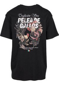 Černé tričko s grafikou dvou kohoutů s detailním peřím. Text zní "Tradición Viva PELEA DE GALLOS."