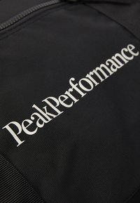 Black fabric bag featuring the text "PeakPerformance" in white, showcasing a textured surface and a zipper closure.