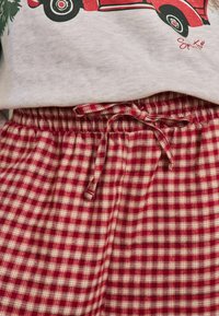 Pantalonii de pijama în carouri roșii și crem au un elastic la talie cu șnur legat. Material moale cu un model în carouri.