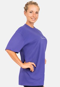 Paarse korte mouwen t-shirt van gladde stof. Heeft een ronde halslijn en een subtiel geborduurd logo op de borst.