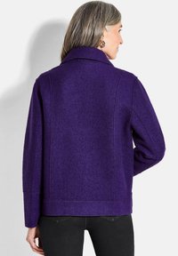 Giacca in misto lana viola con colletto strutturato, dettagli delle cuciture e taglio dritto. Presenta maniche lunghe e una texture liscia.