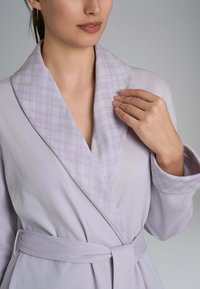 Accappatoio di un leggero color lavanda con un design a quadri sul colletto. Presenta uno stile avvolgente, una cintura e una texture in tessuto morbido.