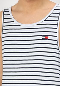 Pruhovaný tílko světle modré a námořnické barvy, vyrobené z měkké tkaniny. Obsahuje malou nášivku s logem "Tommy Jeans" na hrudi. Design s vykrojeným výstřihem na zádech.