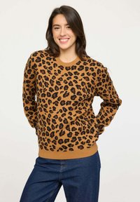 Pull en imprimé léopard dans une teinte beige chaud avec des taches noires, col rond et poignets côtelés. Associé à un jean en denim foncé. Texture en tricot.