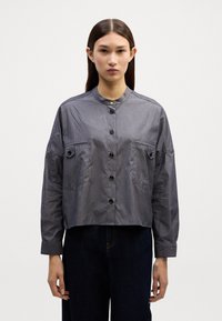 Korte, overhemd in donkerblauw met verticale streepjes. Beschikt over een staande kraag, twee borstzakken en knoopaccenten.